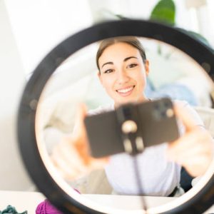 Young Woman Influencer setting up smart phone in ring light for crochet vlog