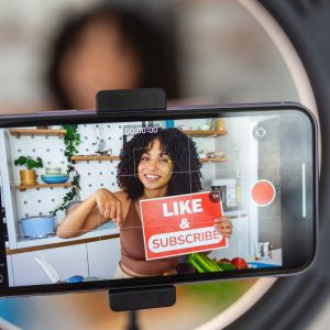 An Afro Caribbean woman showing a creative recipe with healthy fresh ingredients from her kitchen at home, using her smart phone to film the cookery demonstration