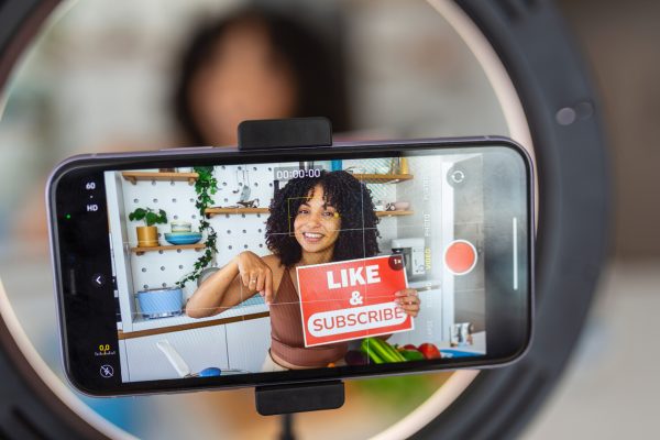 An Afro Caribbean woman showing a creative recipe with healthy fresh ingredients from her kitchen at home, using her smart phone to film the cookery demonstration